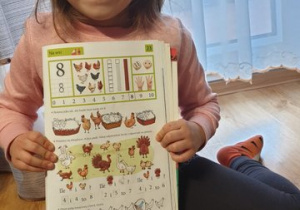 Dziewczynka prezentuje wykonane ćwiczenia w książce